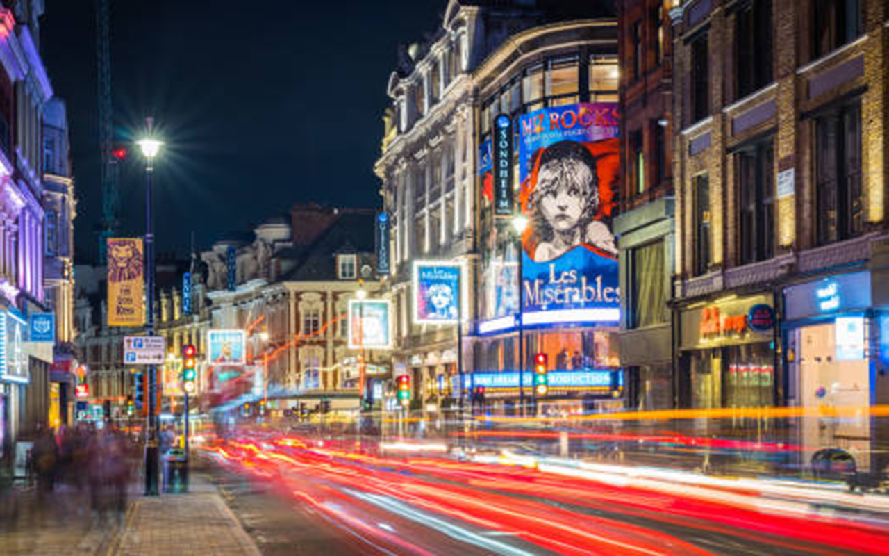 Traffic zooming along Shaftesbury Avenue past the tourist crowds and the billboards of London’s vibrant theatre district at night.