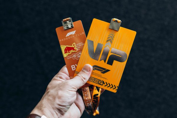 Close-up of a hand holding two VIP event badges against a black background.